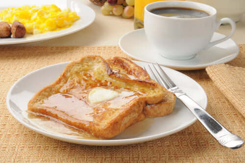 Golden French toast topped with butter and syrup, served with a cup of black coffee and a hearty breakfast spread.