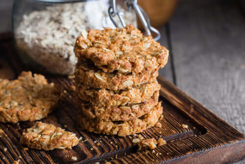 Artisanal oat cookies stacked on a wooden board, with a jar of oats in the background, perfect for indulgent snacking.